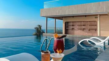 An infinity pool with a clear view of the ocean, a modern building with large windows, and two lounge chairs.