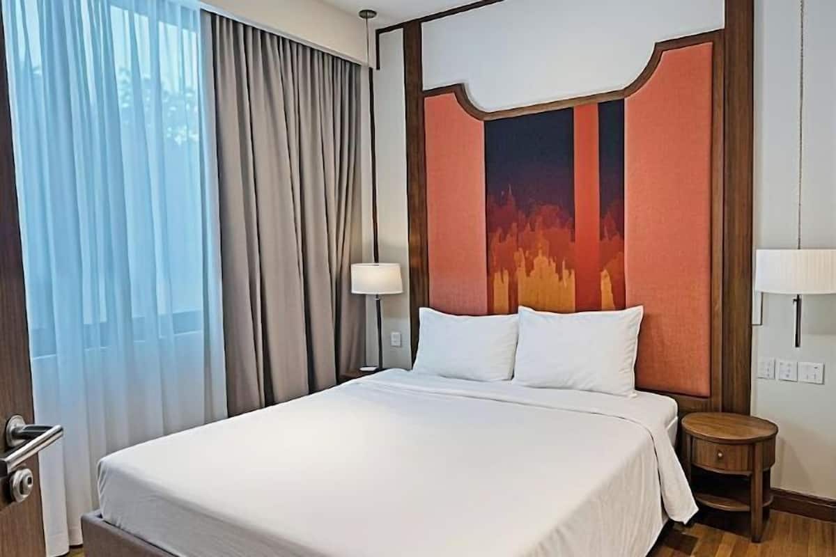 Une chambre d’hôtel avec un grand lit, une table de chevet, une lampe et une vue sur la ville par la fenêtre.