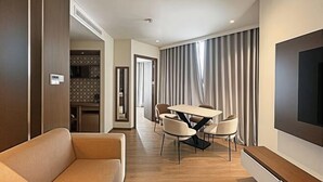 Une chambre d’hôtel moderne équipée d’un canapé, d’une table à manger avec des chaises, d’un téléviseur à écran plat et d’une grande fenêtre avec des rideaux.
