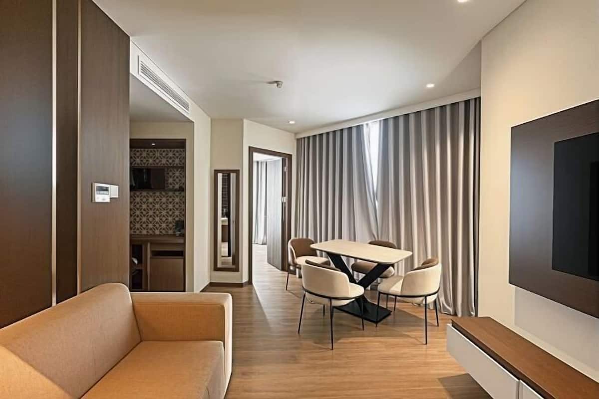 Une chambre d’hôtel moderne équipée d’un canapé, d’une table à manger avec des chaises, d’un téléviseur à écran plat et d’une grande fenêtre avec des rideaux.