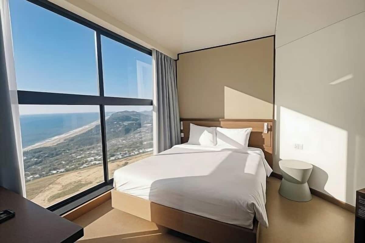 Une chambre d’hôtel dotée d’une grande fenêtre, d’un lit, d’une table de chevet et d’une chaise au design moderne.