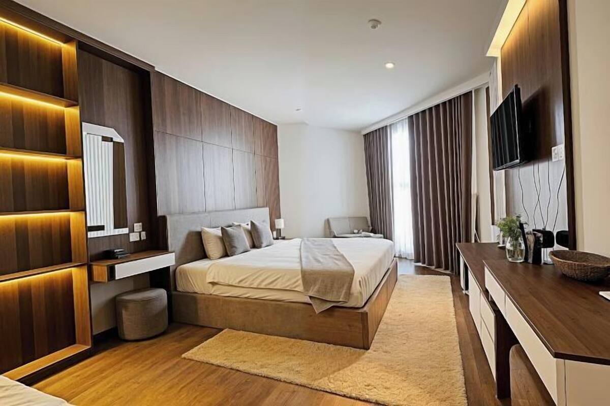 Une chambre moderne avec un grand lit, des tables de chevet, un téléviseur intégré et un mur d’accent en bois.