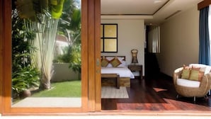 A bedroom with a bed, bedside table, and a wicker chair. - Villa Haineu (Koh Samui)