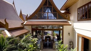 A traditional building with a sloped roof, a central entrance with glass doors, and a courtyard with plants and seating. - Villa Haineu (Koh Samui)