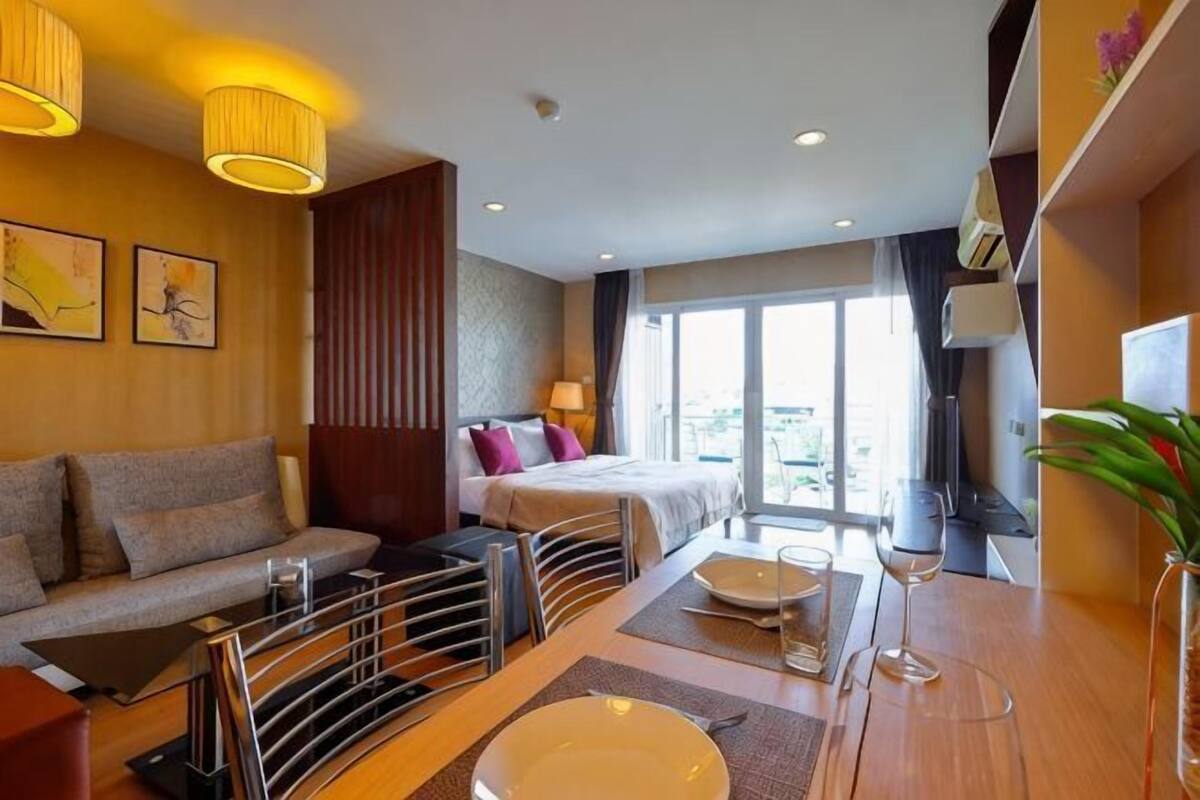 A hotel room with a sofa, a bed, a dining table with chairs, and a large window.