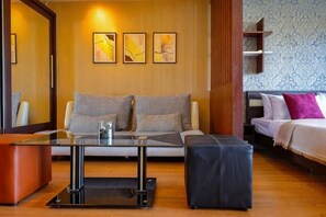 A hotel room with a sofa, a glass-top table, a bed, and a wooden floor. - Luxury Living in heart of Nimman (Chiang Mai)