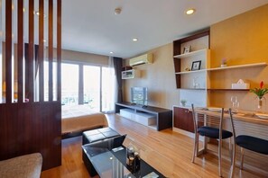A modern hotel room with a bed, a TV, a dining area, and a view of the outdoors.