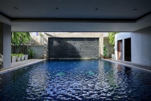 A swimming pool with a stone wall, surrounded by a modern building with a flat roof and minimalistic design.
