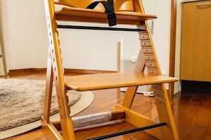 A wooden chair with a black strap and a shelf, placed on a wooden floor with a rug. - Mizunowa (Nago)