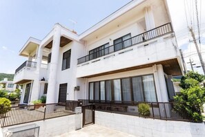 Un edificio residencial de dos pisos con balcones, grandes ventanales y una entrada protegida por una reja.