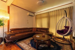 A living room with a sectional sofa, a round coffee table, a hanging chair, and a patterned rug. - Mizunowa (Nago)