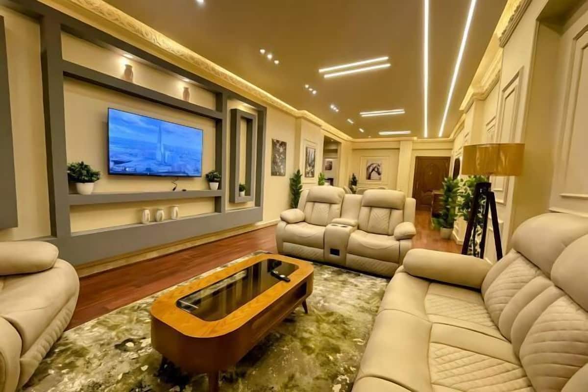 A modern living room with a flat-screen TV, leather sofas, a coffee table, and a ceiling with recessed lighting.