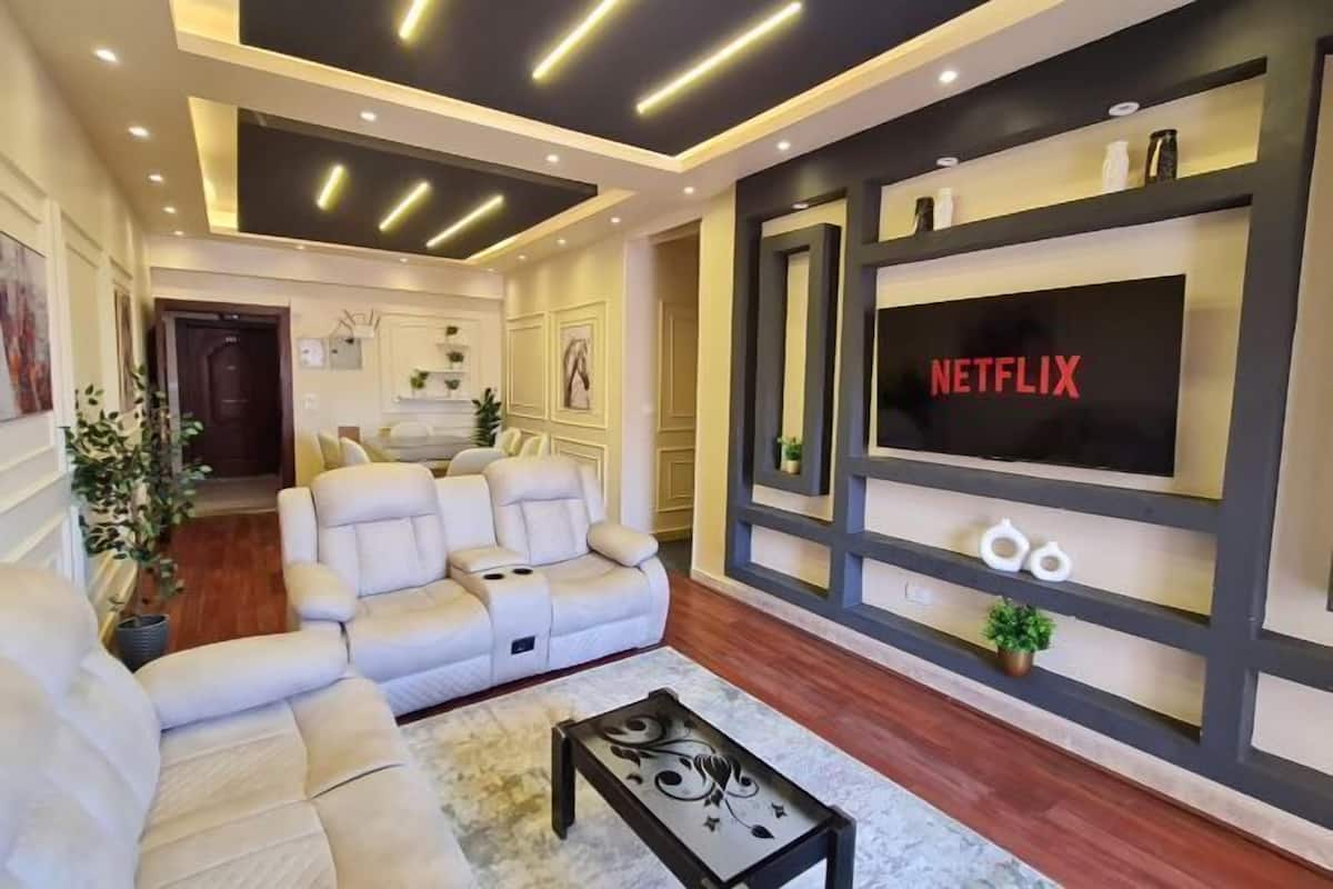 A modern living room with a sofa, a coffee table, and a wall-mounted TV displaying 'NETFLIX'.