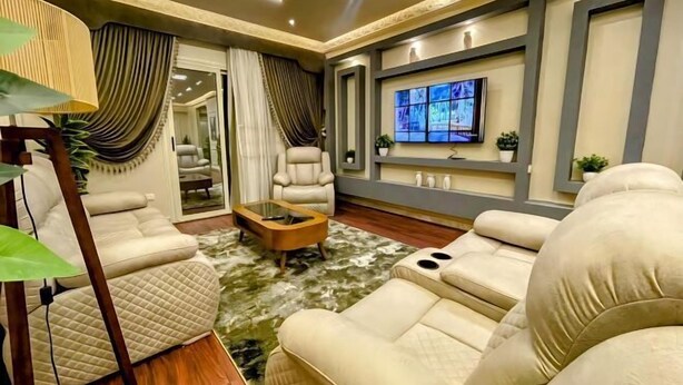 A modern living room with a sofa set, a coffee table, a TV mounted on the wall, and a large window with curtains. - RD The Residence Serviced Apartment, New Cairo Prime Location (New Cairo City)