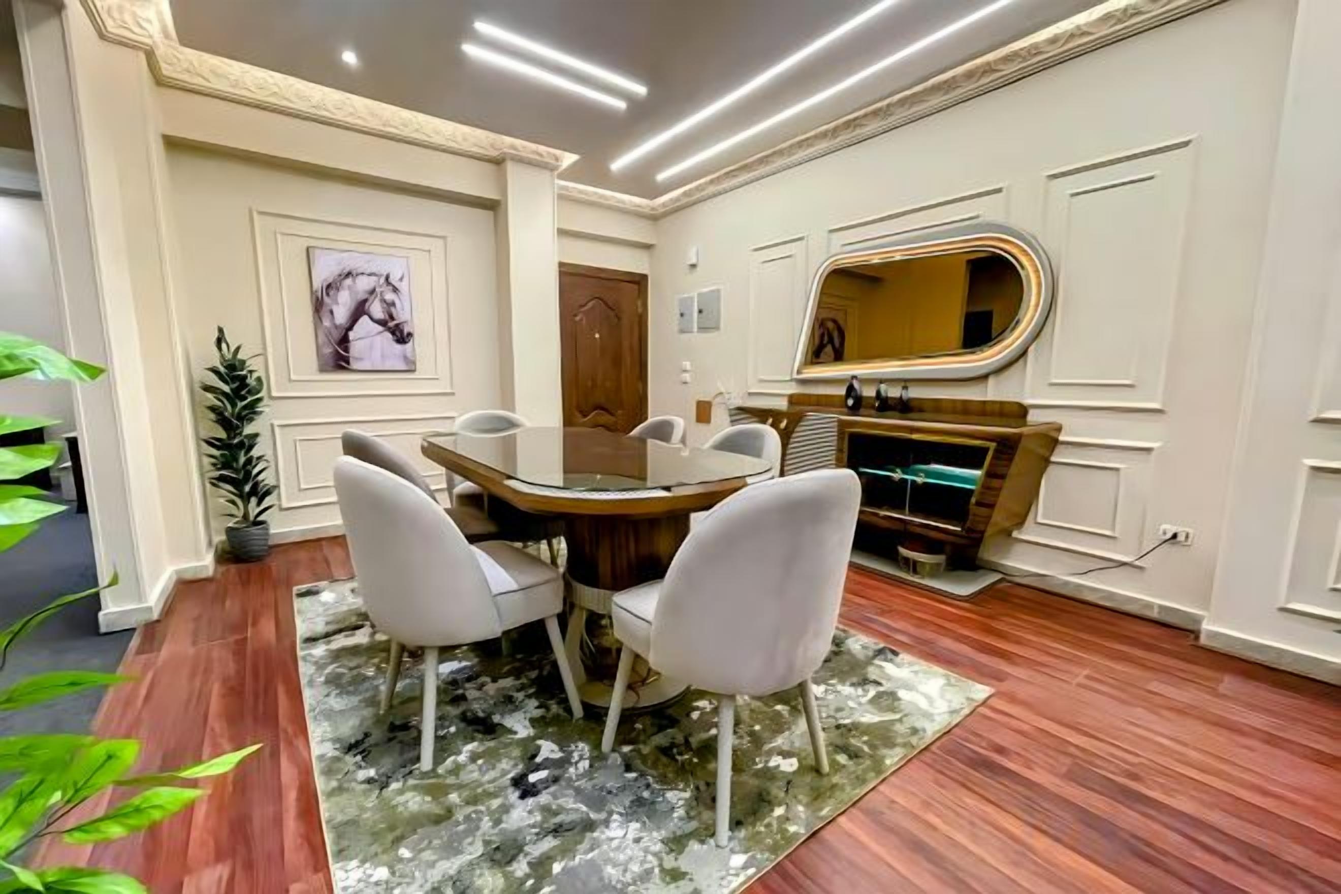 A dining area with a round table, chairs, a rug, and a mirror on the wall.