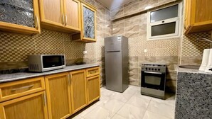 A kitchen with wooden cabinets, a microwave, a refrigerator, and an oven. - RD The Residence Serviced Apartment, New Cairo Prime Location (New Cairo City)