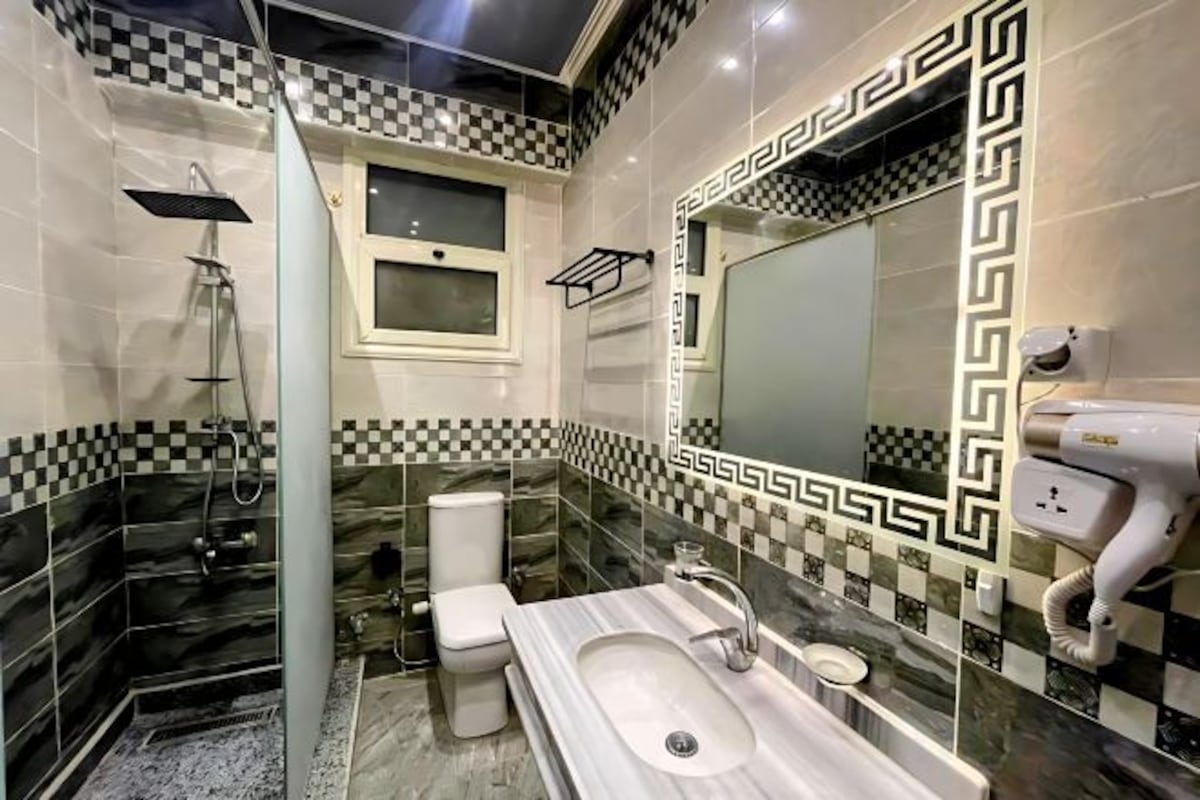 A bathroom with a checkered floor, a large mirror, a sink, and a toilet.