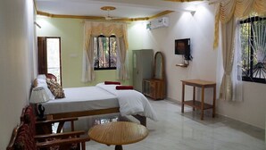 A bedroom with a bed, a wooden table, a mirror, and a TV. - Pritams Cottages (Canacona)