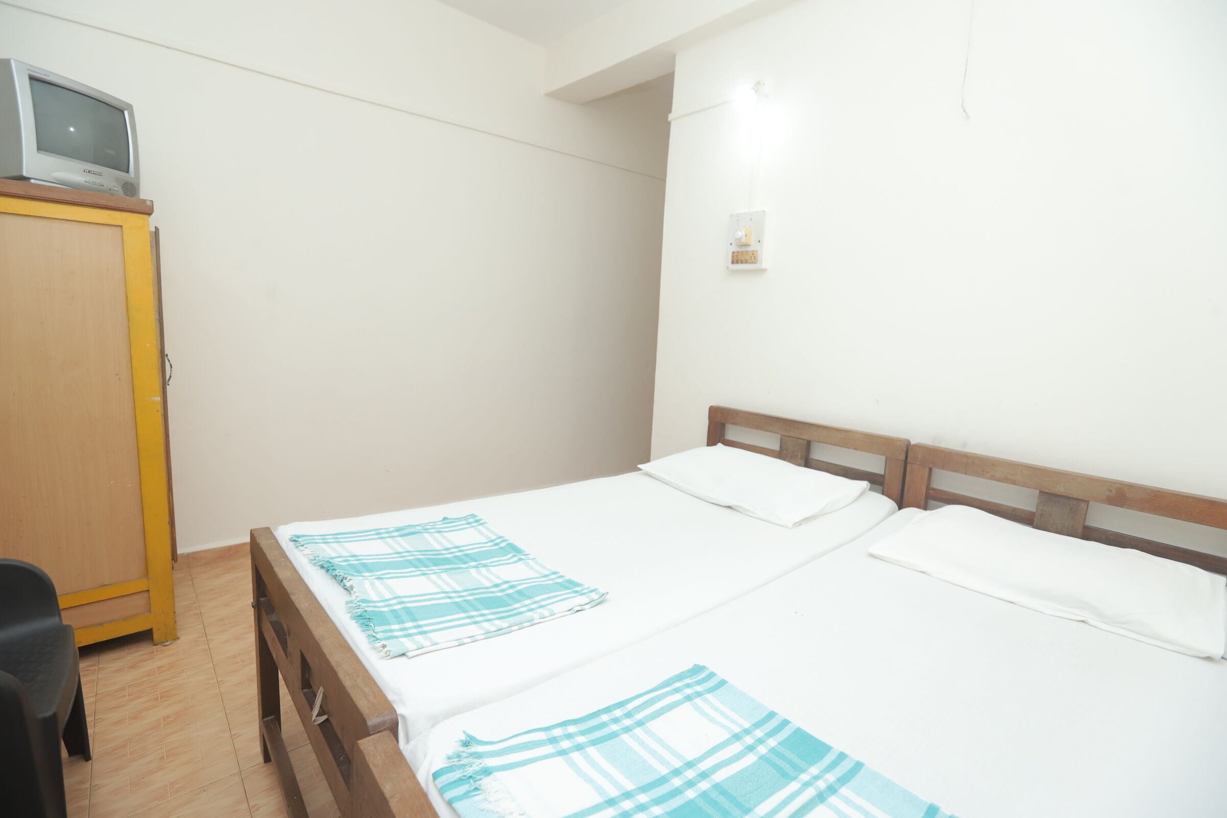 A single-bed room with a wooden headboard, a small television on a cabinet, and a plain white wall.