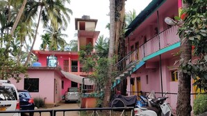 A pink two-story building with a balcony, parked cars, and a scooter. - Pritams Cottages (Canacona)