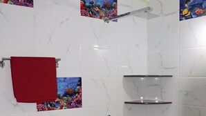 Un baño con azulejos de mármol blanco, una ducha con accesorios cromados, una toalla roja y obras de arte con motivos de vida marina de colores en las paredes.