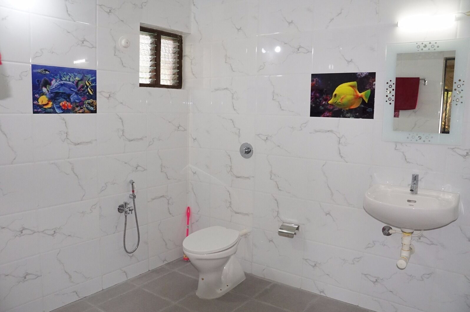 A bathroom with a toilet, a sink, and a shower. There are two wall-mounted pictures, one of a fish and one of a coral reef.