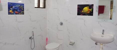 A bathroom with a toilet, a sink, and a shower. There are two wall-mounted pictures, one of a fish and one of a coral reef.