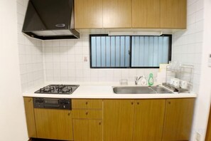 A kitchen with a gas stove, dishwasher, and a window with blinds. - SunStay Osaki I (Tokyo)