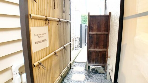 A narrow hallway with a bamboo screen, a wooden door, and a stone floor. - SunStay Osaki I (Tokyo)