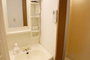 A bathroom with a white sink, a mirror, a shelf with toiletries, and a towel rack. - SunStay Osaki I (Tokyo)