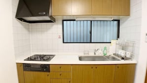 A kitchen with a gas stove, dishwasher, wooden cabinets, a window with blinds, and a sink. - SunStay Osaki I (Tokyo)