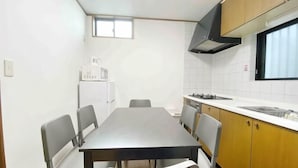 A compact kitchen with a dining table, chairs, a refrigerator, and a window. - SunStay Osaki I (Tokyo)