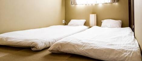 A room with two single beds, a bedside table, and a window with curtains.