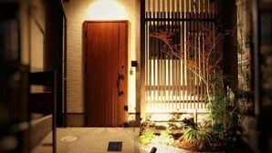 A wooden door with a metal gate, a small garden with plants, and a light fixture above the door. - KIRAKU･KAYA (Kyoto)