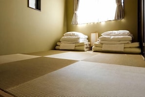 A room with tatami mats, a bed with neatly folded white bedding, and a window with curtains.