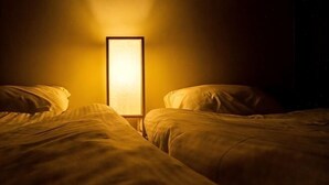 A hotel room with two beds, a nightstand, and a wall-mounted lamp. - KIRAKU･KAYA (Kyoto)