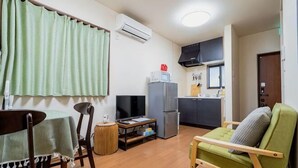 A compact living space with a dining table, a green sofa, a kitchen area with a refrigerator, and a television. - KIRAKU･KAYA (Kyoto)