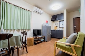 A compact living space with a dining table, a green sofa, a kitchen area with a refrigerator, and a television. - KIRAKU･KAYA (Kyoto)