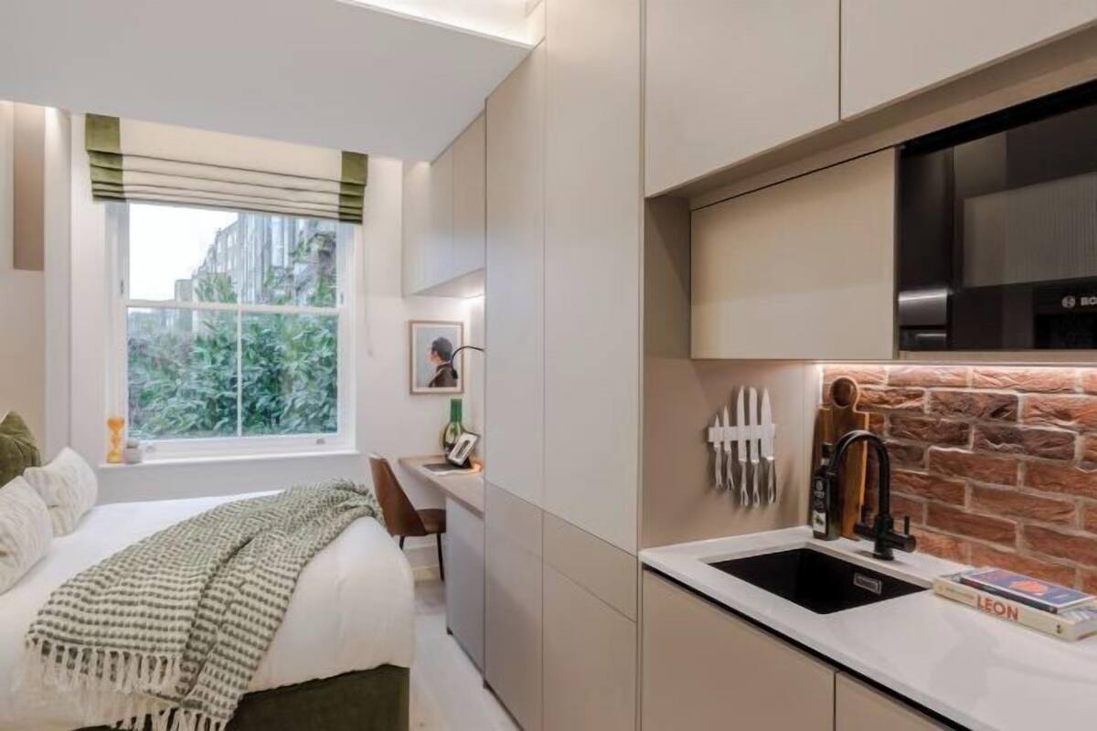 A modern kitchen with a built-in stove, a sink, and a window with a view of greenery.