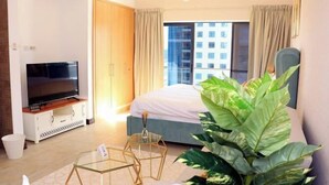 A modern hotel room with a large bed, a TV on a wooden cabinet, a glass coffee table, and a large plant. - Gcv1 (Dubai)