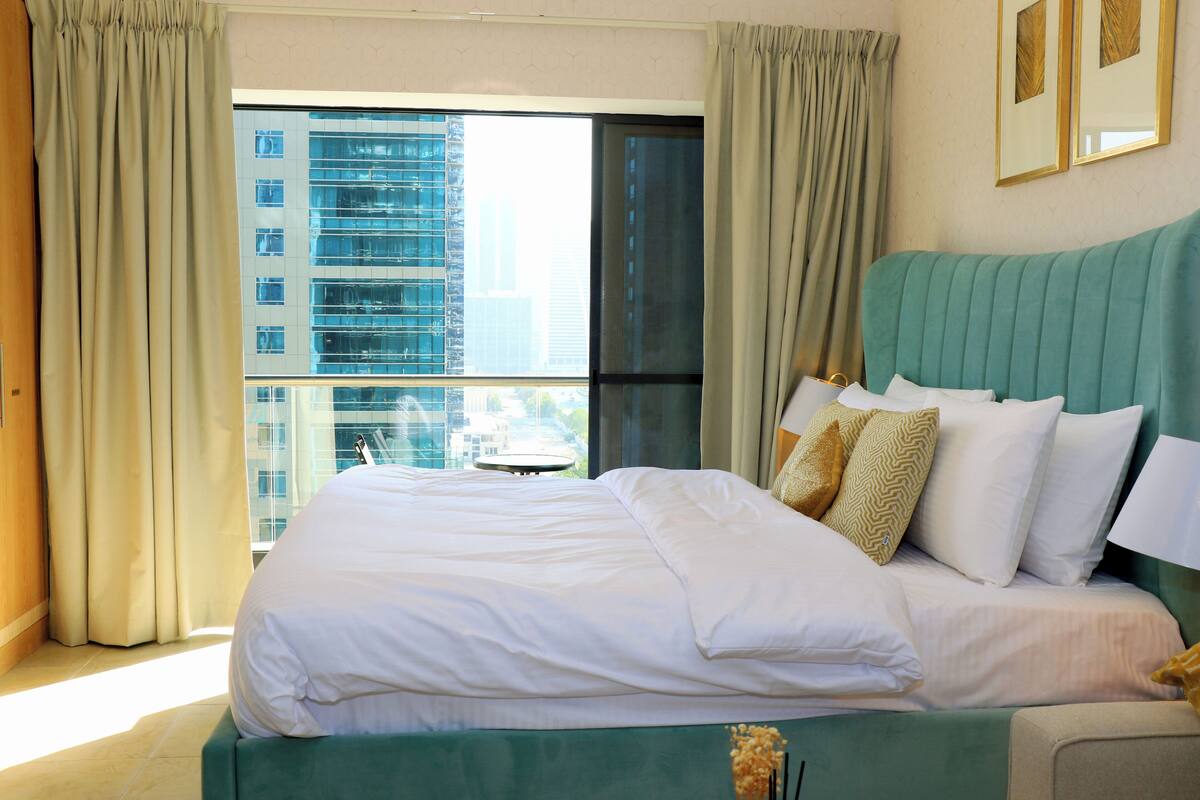 A hotel room with a large bed, a view of a cityscape, and a window with curtains.