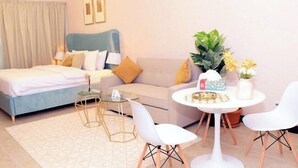 A bedroom with a bed, a sofa, a small table, chairs, and a potted plant. - Gcv1 (Dubai)