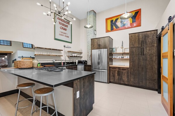 Una cocina moderna con una isla central, taburetes de bar, un refrigerador de acero inoxidable y armarios de madera.