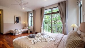 Une chambre à coucher avec un grand lit, une table de chevet, une chaise, une fenêtre avec des rideaux et un ventilateur de plafond.