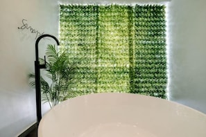 A bathroom with a bathtub, a green wall with a vertical garden, and a black metal chair.