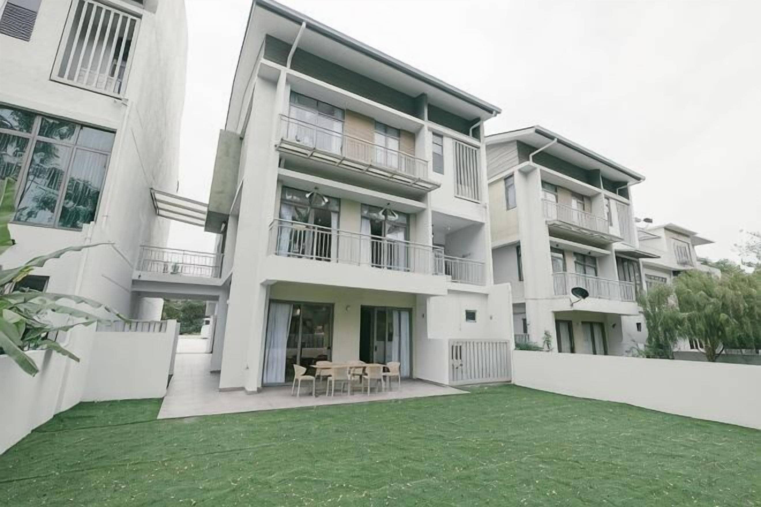 A modern multi-story residential building with balconies, a covered patio, and a well-maintained lawn.