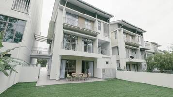 A modern multi-story residential building with balconies, a covered patio, and a well-maintained lawn.