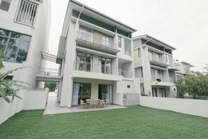 A modern multi-story residential building with balconies, a covered patio, and a well-maintained lawn.