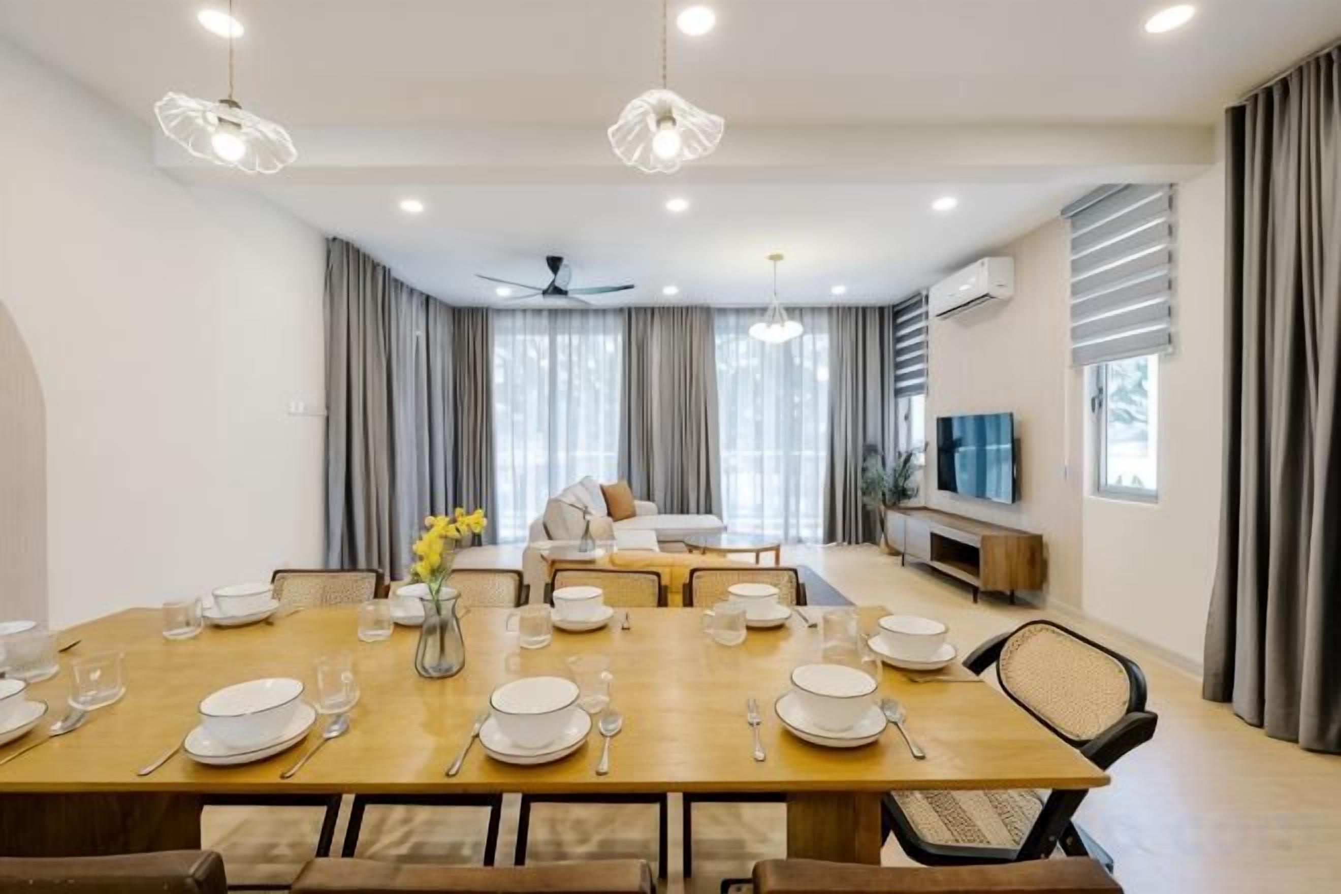 A dining area with a wooden table set for a meal, a ceiling fan, and a TV on the wall.