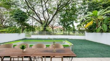 An outdoor patio with a wooden table and chairs, surrounded by greenery and a white fence.
